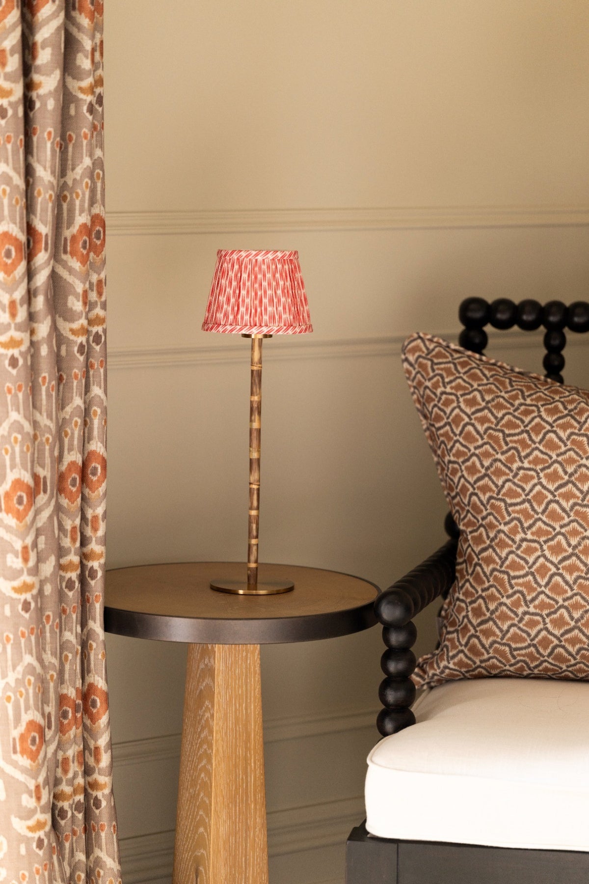 Red ikat pleated shade on a bamboo table lamp, beside a bobbin chair with a patterned cushion